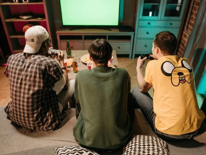 Three young men enjoying a home gaming session together, playing video games in a cozy indoors setting.